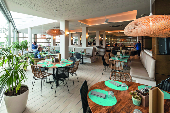 Blick in ein Restaurant mit braunen Tischen und Korbstühlen